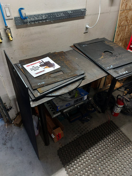 Construction plans for an offset smoker that are sitting on a stack of steel parts.